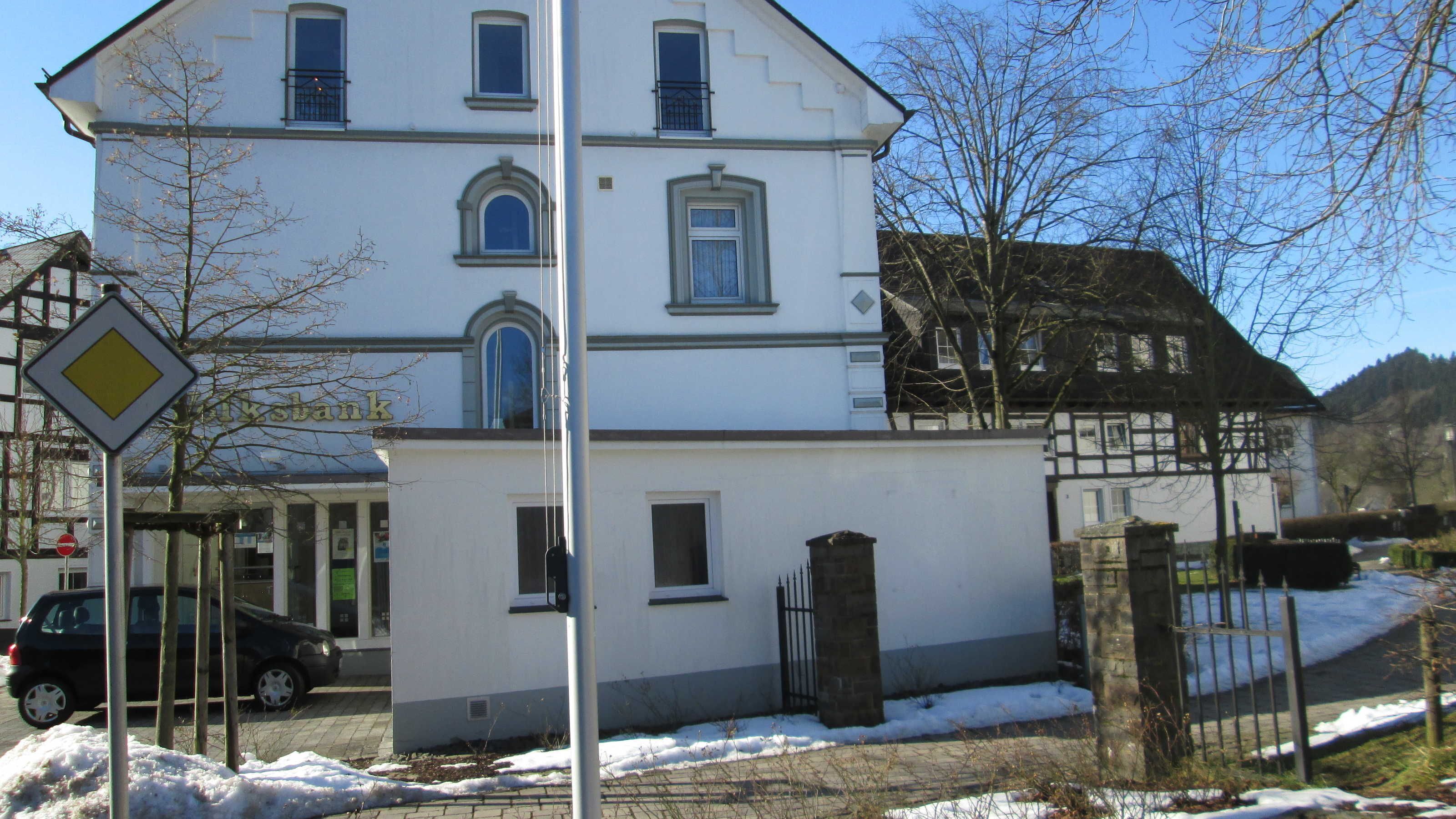 A two-story building with a white facade, multiple windows, and a visible entrance.