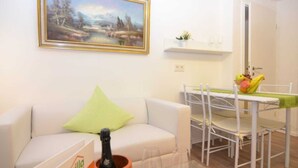 Una sala de estar con un sofá blanco, un cojín verde, una mesa con copas de vino y un cuadro en la pared.