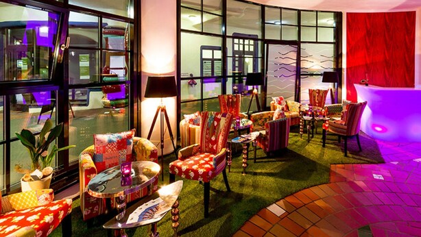Een moderne hotel lobby met een gebogen zithoek, grote ramen en een rode accentmuur.