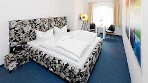 Een hotelkamer met een groot bed, een bureau, twee stoelen, een lamp en een uitzicht op een stadsbeeld door het raam.