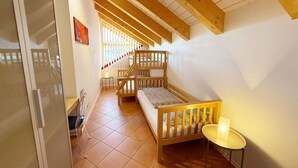 A room with a bunk bed, a small table, and a staircase leading to an upper level.