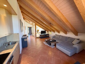 A modern loft with a kitchen, a living area with a sofa and TV, and a high ceiling with exposed beams.