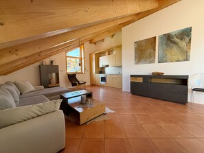 Ein moderner Loftsitz mit schrägverdachter Decke, einer Couch, einem Couchtisch und einer Küchenzeile.