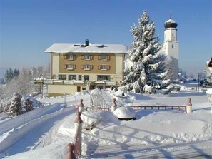Un bâtiment dont le toit est recouvert de neige, avec un grand arbre et une tour.