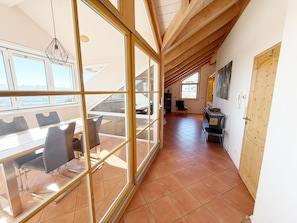 Ein geräumiges Zimmer mit einer großen Schiebeglastür, die auf eine Terrasse führt, einem Essbereich mit Tisch und Stühlen sowie einer Küchenzeile mit Herd und Spüle.