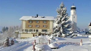 A building with a snow-covered roof, a large tree, and a tower.