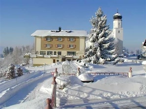 Ein Gebäude mit verschneietem Dach, einem großen Baum und einem Turm.
