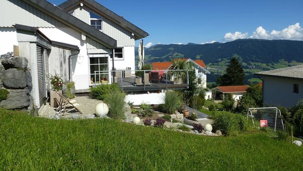 Une maison moderne dotée d’un grand jardin, d’une terrasse et offrant une vue sur les montagnes.