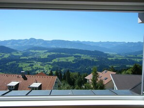 Ein Blick über ein Tal mit Bergen im Hintergrund, ein Haus mit rotem Dach und Bäume.