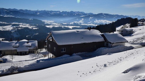 A snow-covered mountain village with traditional houses and a clear view of distant peaks.