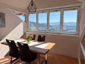 A dining area with a table, chairs, and a view of mountains through a large window.