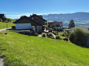 A residential area with two houses on a hillside, surrounded by greenery and a clear view of distant mountains.