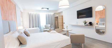 Ett modernt hotellrum med en stor säng, en sittgrupp med bord och stolar, en TV som är monterad på väggen och en spegel.