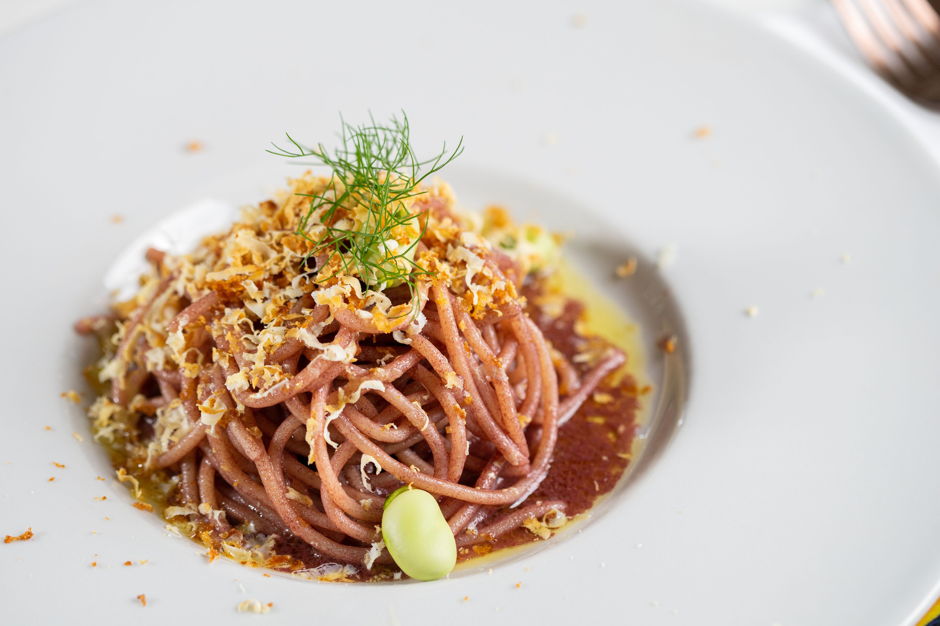 A plate of spaghetti with a garnish of green herbs and grated cheese.