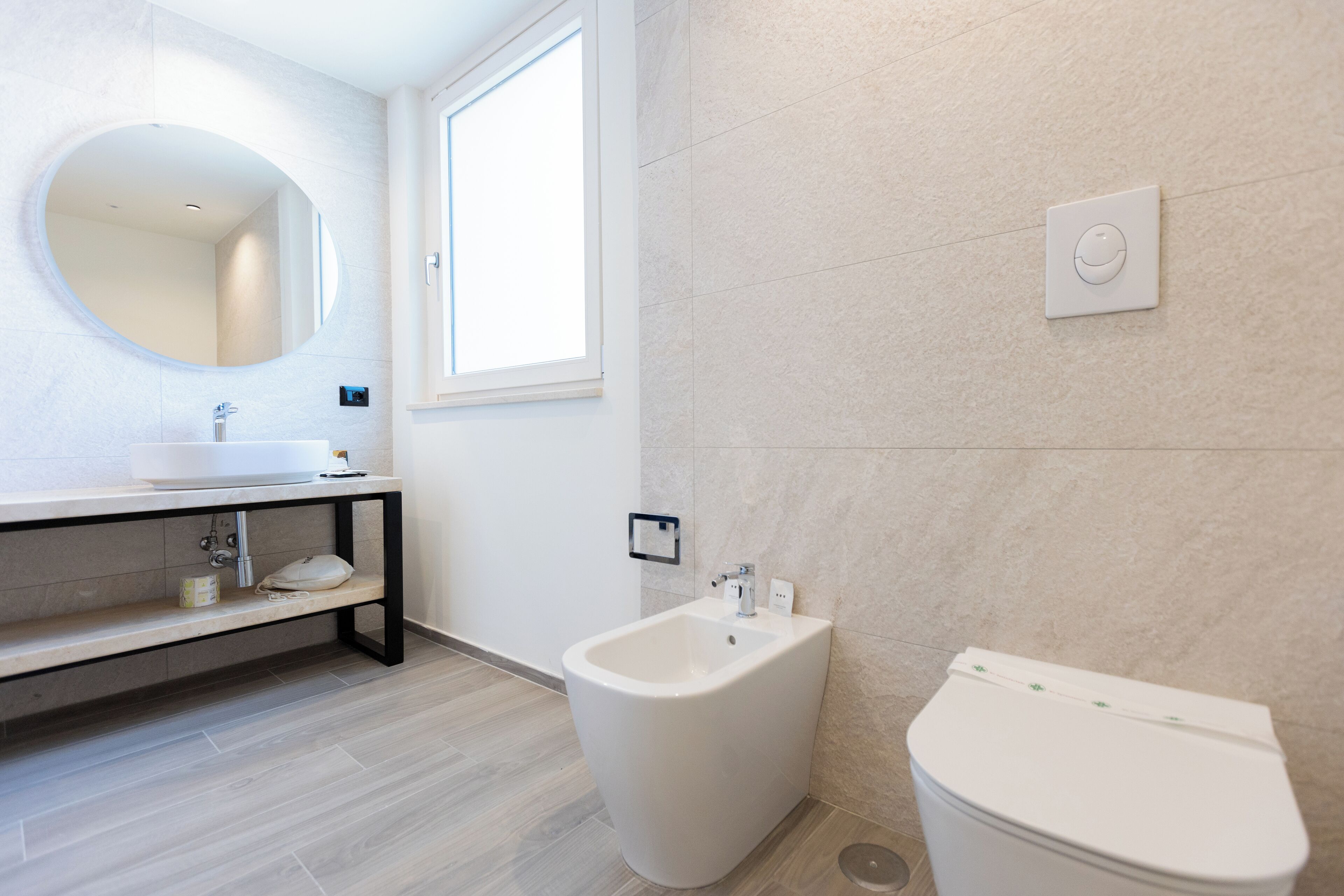 A modern bathroom with a round mirror, a sink, a bidet, and a toilet.