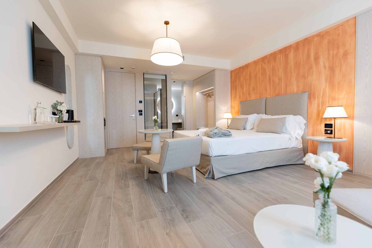 Une chambre d’hôtel moderne équipée d’un lit, de tables de chevet, d’un bureau, d’une chaise, d’une télévision et d’un miroir.