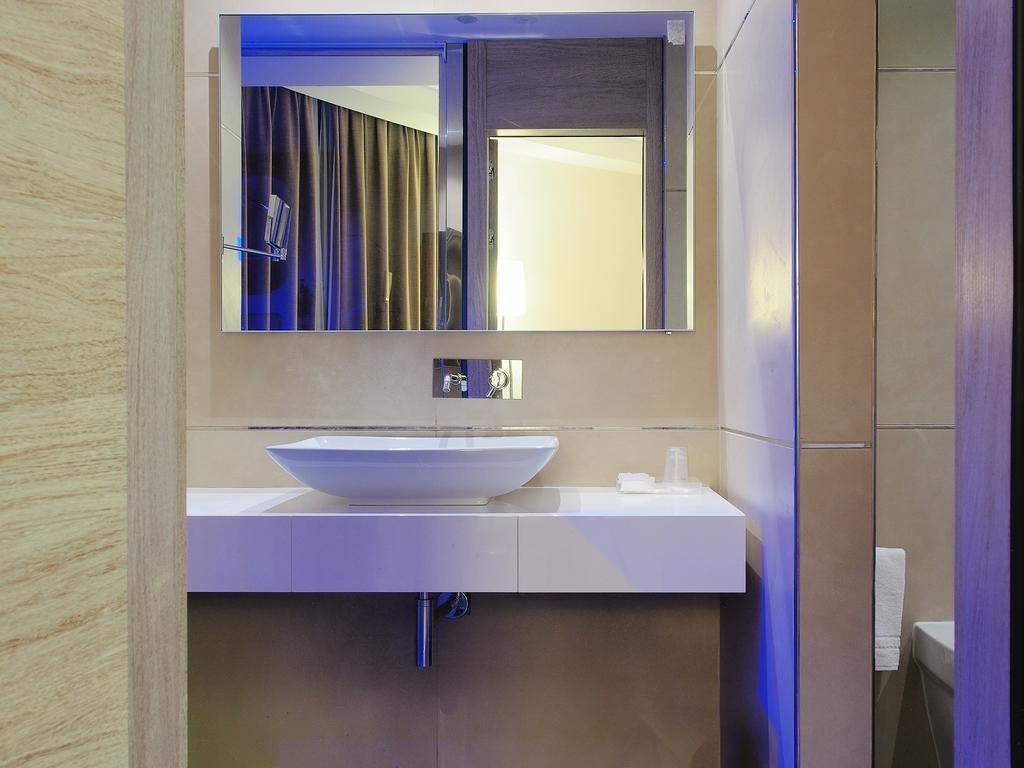 Un baño moderno con un espejo grande, un lavamanos blanco y un perchero para toallas.