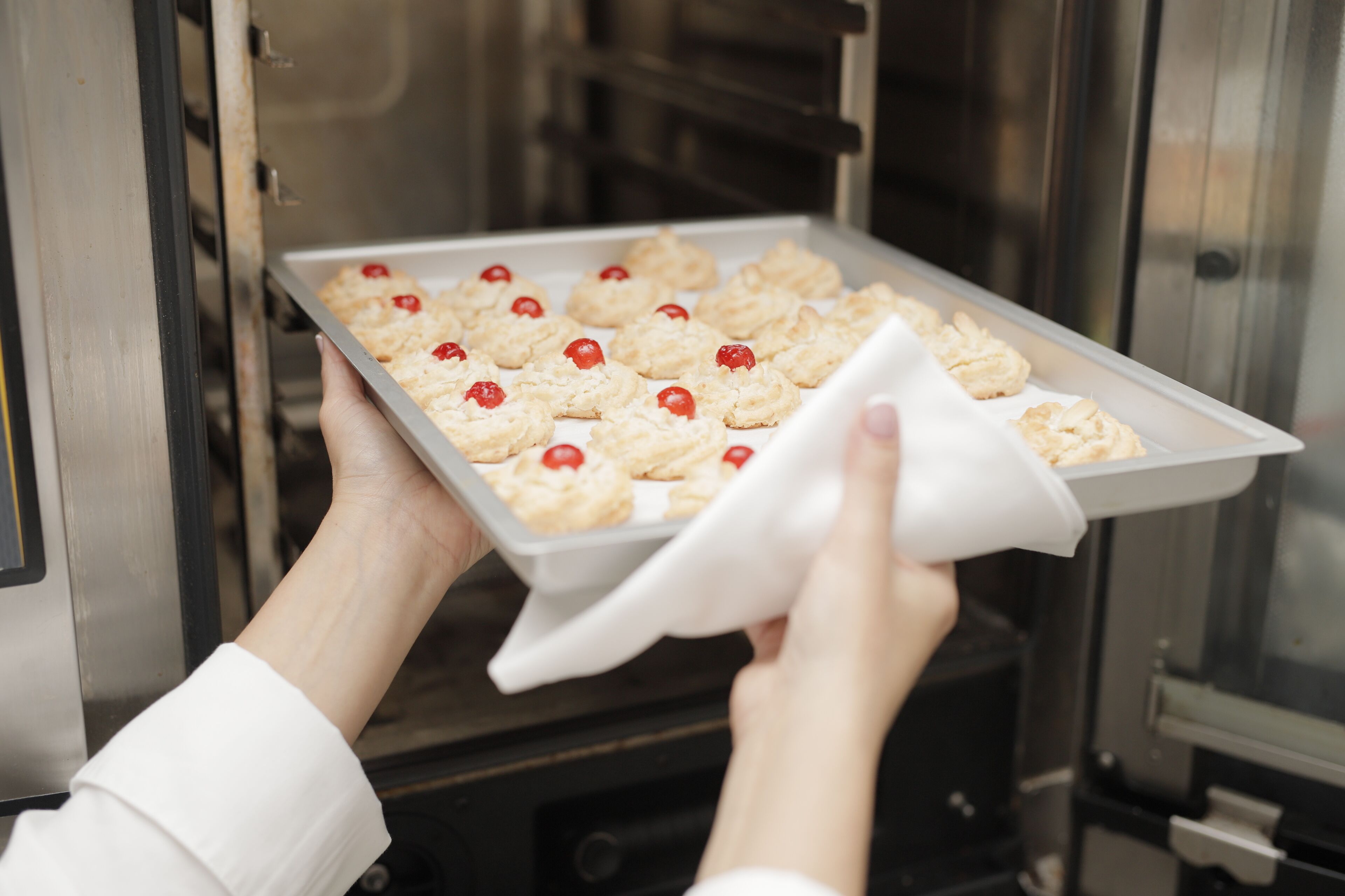 Una persona sosteniendo una bandeja de galletas con cerezas.