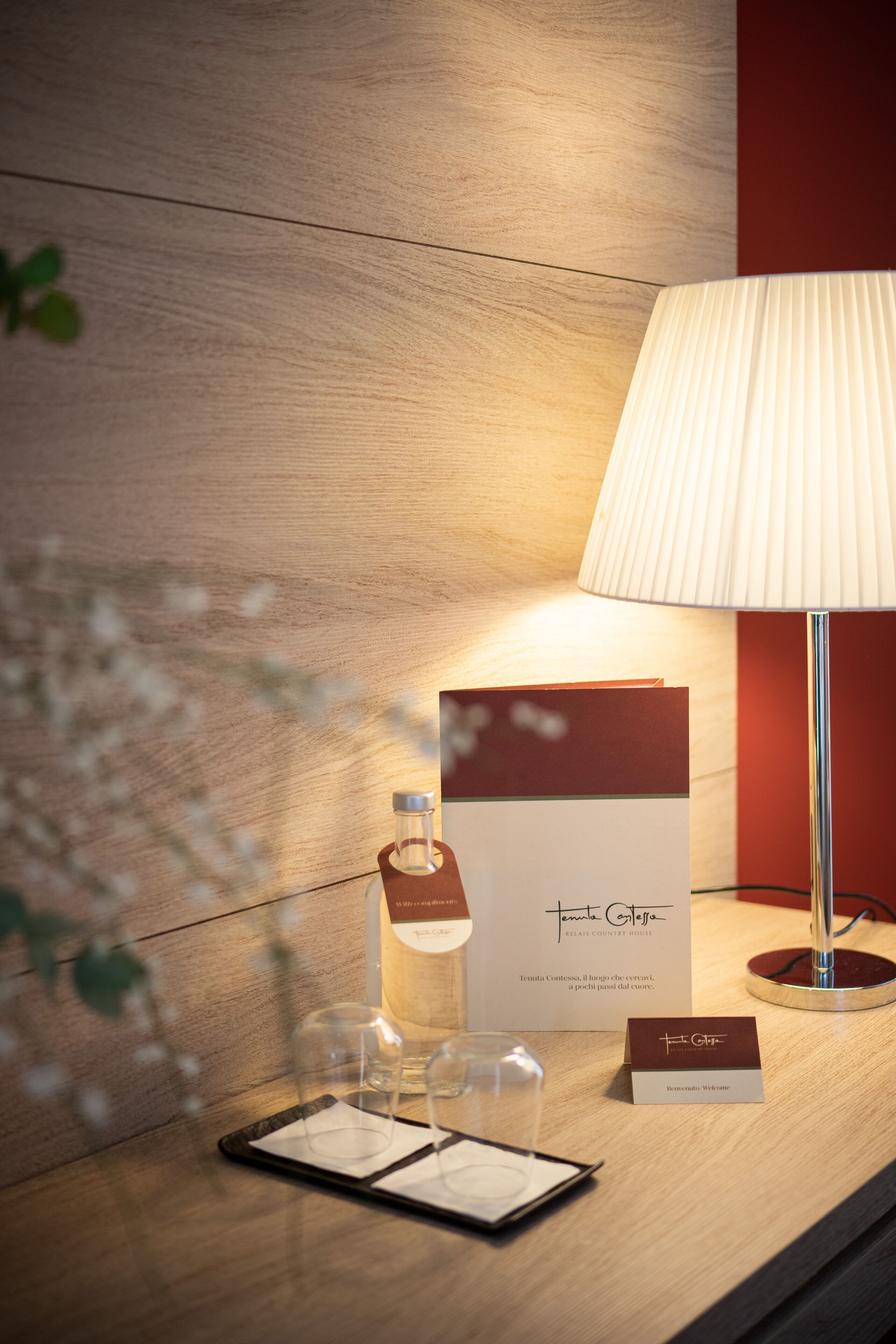 A hotel reception desk with a lamp, a bottle, glasses, a menu, and a name card.
