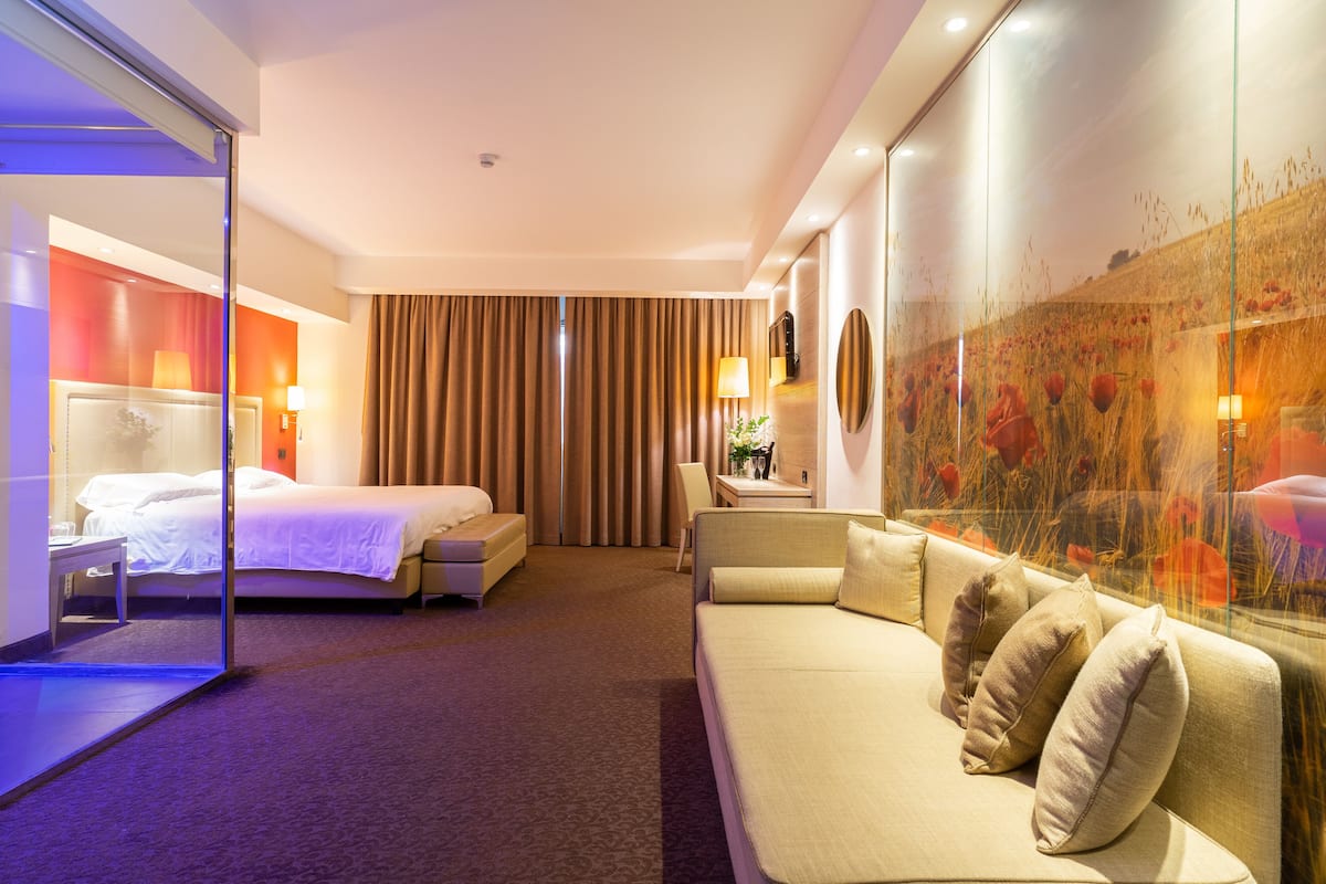 Une chambre d’hôtel avec un lit, un canapé, un bureau et une grande fenêtre donnant sur un champ.