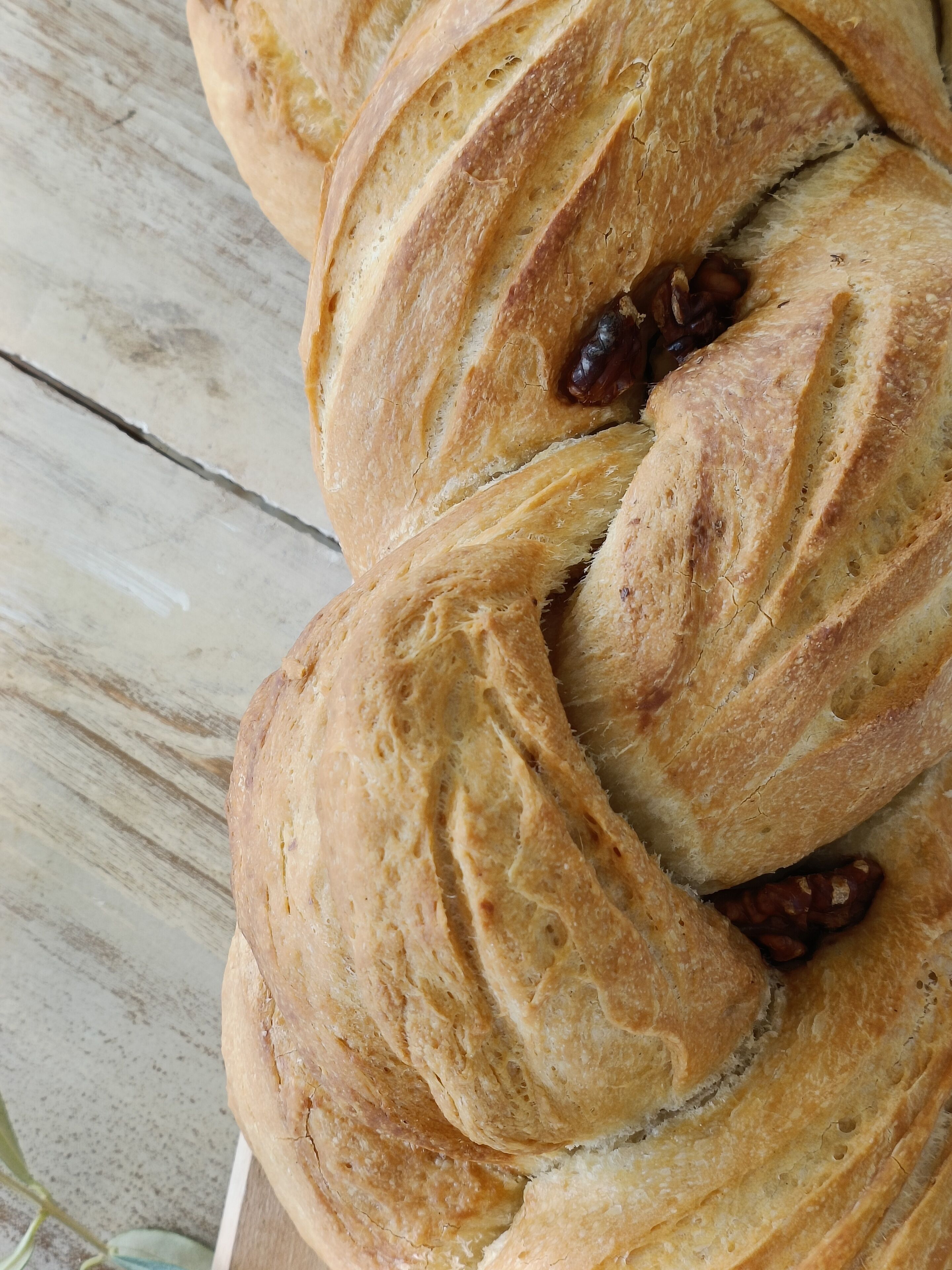 A loaf of braided bread with raisins on a wooden surface.