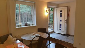 A dining area with a round table, chairs, a window with curtains, and a door with a handle.