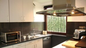 A modern kitchen with stainless steel appliances, white cabinets, and a window with a view of greenery.