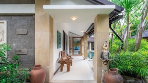 A pathway leading to a building with a stone facade, wooden benches, and large vases. - Villa Aveli Seminyak by Best Deals Asia Hospitality (Seminyak)