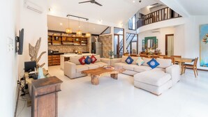 A spacious living room with a high ceiling, a wooden coffee table, two sofas, a dining area, and a kitchen in the background. - Villa Aveli Seminyak by Best Deals Asia Hospitality (Seminyak)