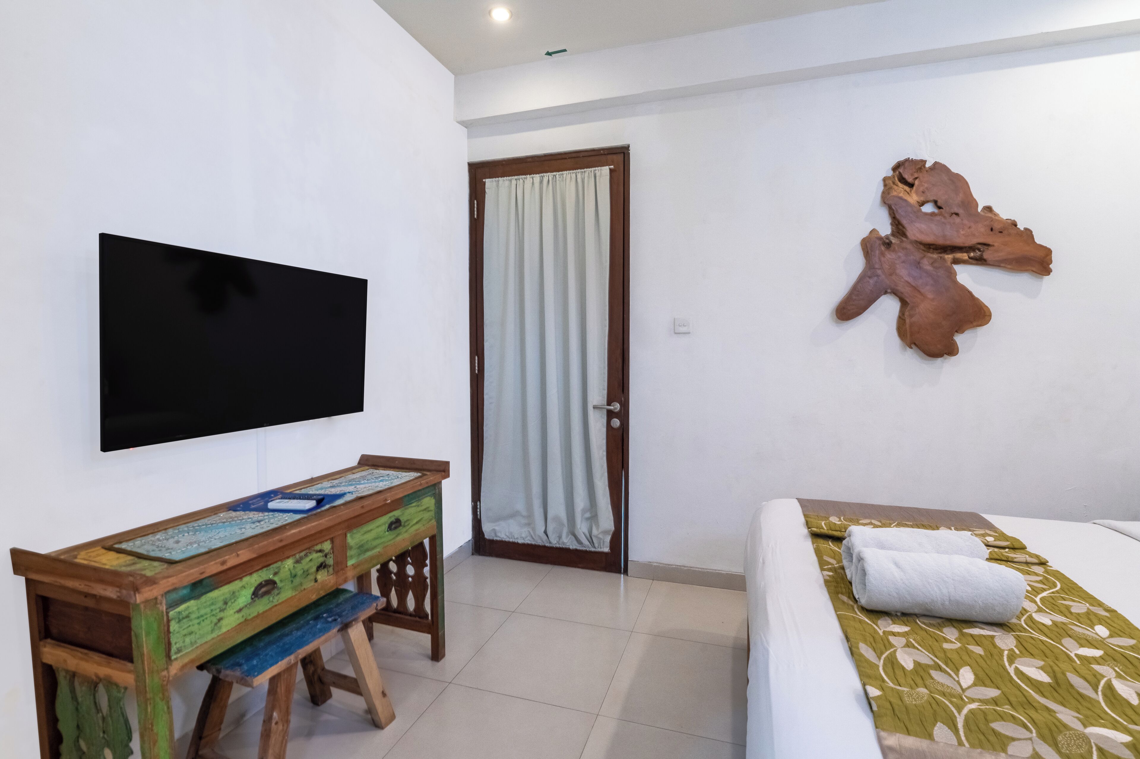 Habitación de hotel con cama, televisor montado en la pared, escritorio de madera y una puerta con cortina.
