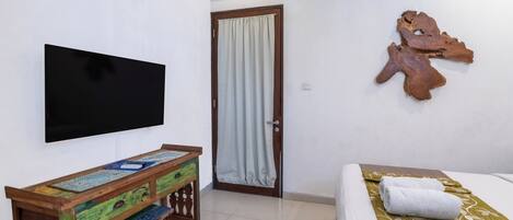 Habitación de hotel con cama, televisor montado en la pared, escritorio de madera y una puerta con cortina.