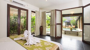 A hotel room with a bed, a view of a pool, and a balcony with a table and chairs. - Villa Aveli Seminyak by Best Deals Asia Hospitality (Seminyak)