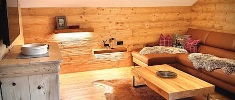 Una habitación acogedora con paredes de madera, un sofá de cuero marrón, una mesita de madera y una pequeña figura de ciervo.
