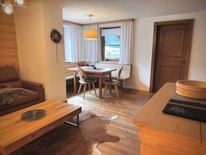 Una sala acogedora con una mesa de madera, un sofá de cuero, una mesa de comedor con sillas, una puerta de madera y un ventanal con cortinas.