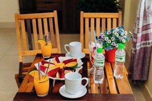 A wooden table with a fruit platter, two white cups, a glass of orange juice, and two Dasani water bottles. - Thanh Phat Phong Nha (Phong Nha)