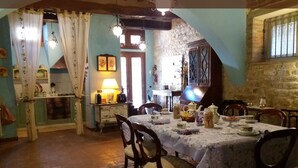 Un comedor con una mesa lista para cuatro personas, rodeada de sillas. Se ve un área de cocina con estufa y armarios a la izquierda.