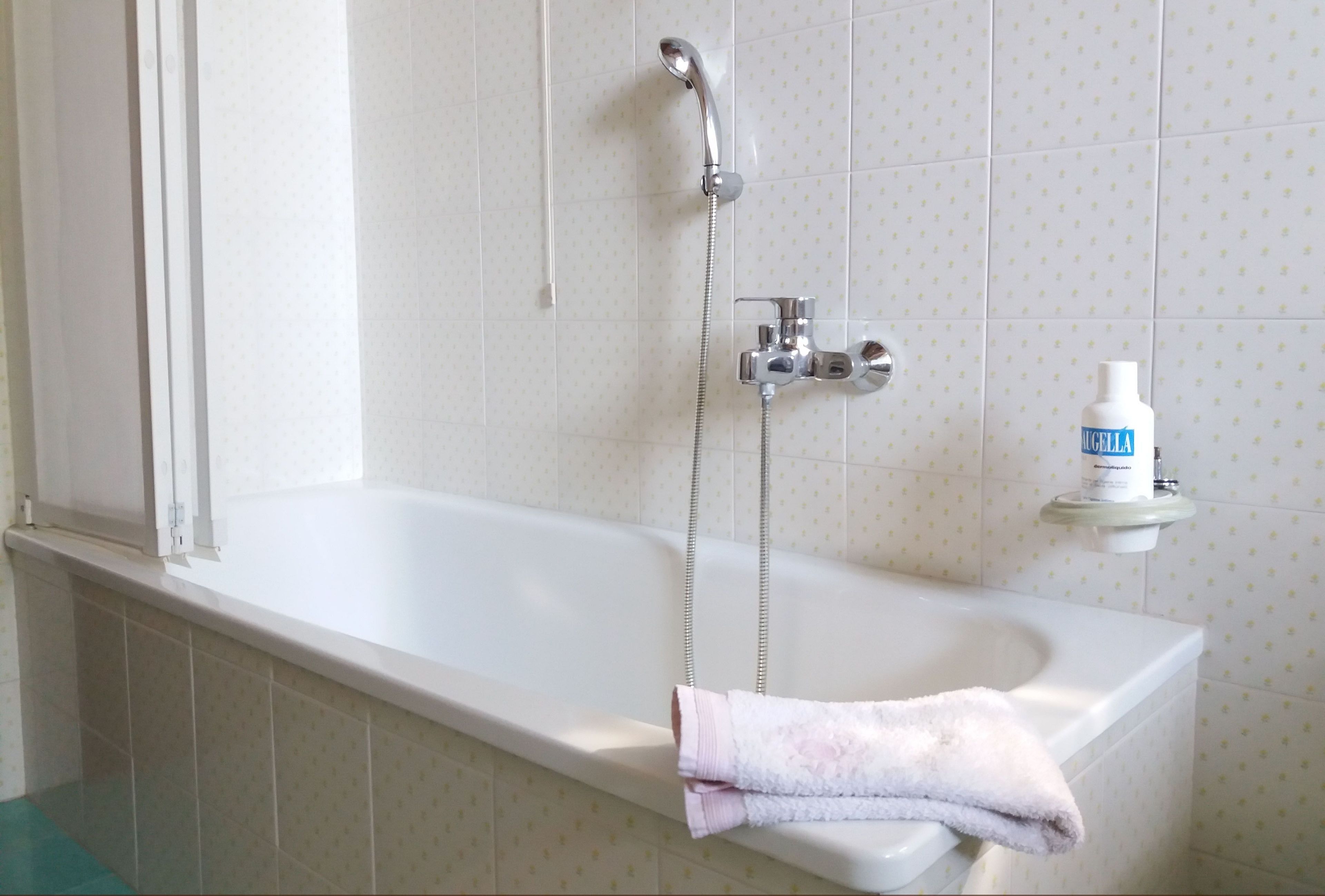 A bathroom with a bathtub, a shower, and a hand soap dispenser on a shelf.