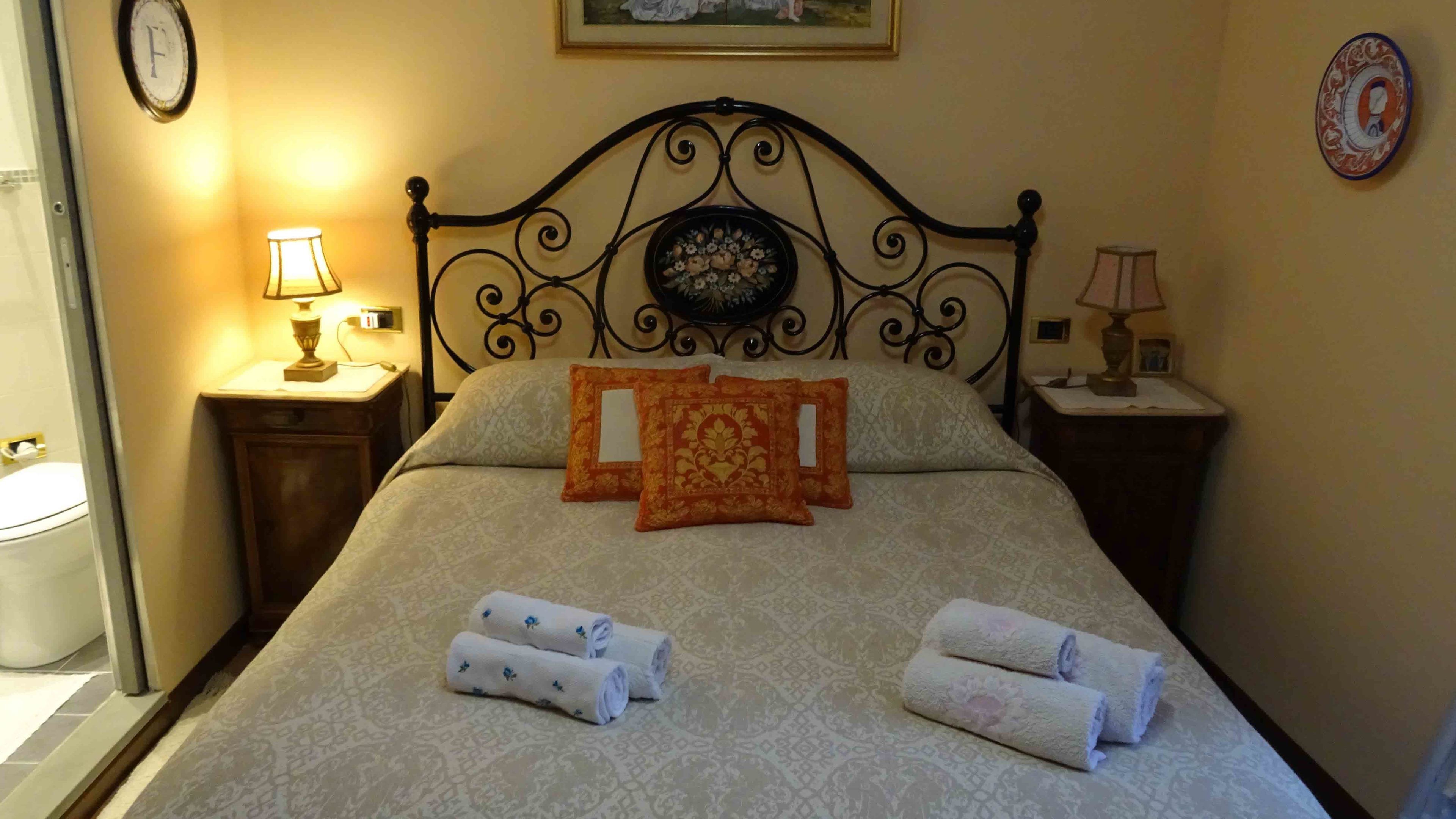 Una cama bien hecha con una colcha estampada, dos almohadas decorativas y toallas enrolladas.