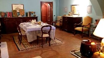 A dining area with a table set for four, surrounded by wooden chairs. A radiator is visible in the background, and a wooden cabinet with decorative items is to the left.