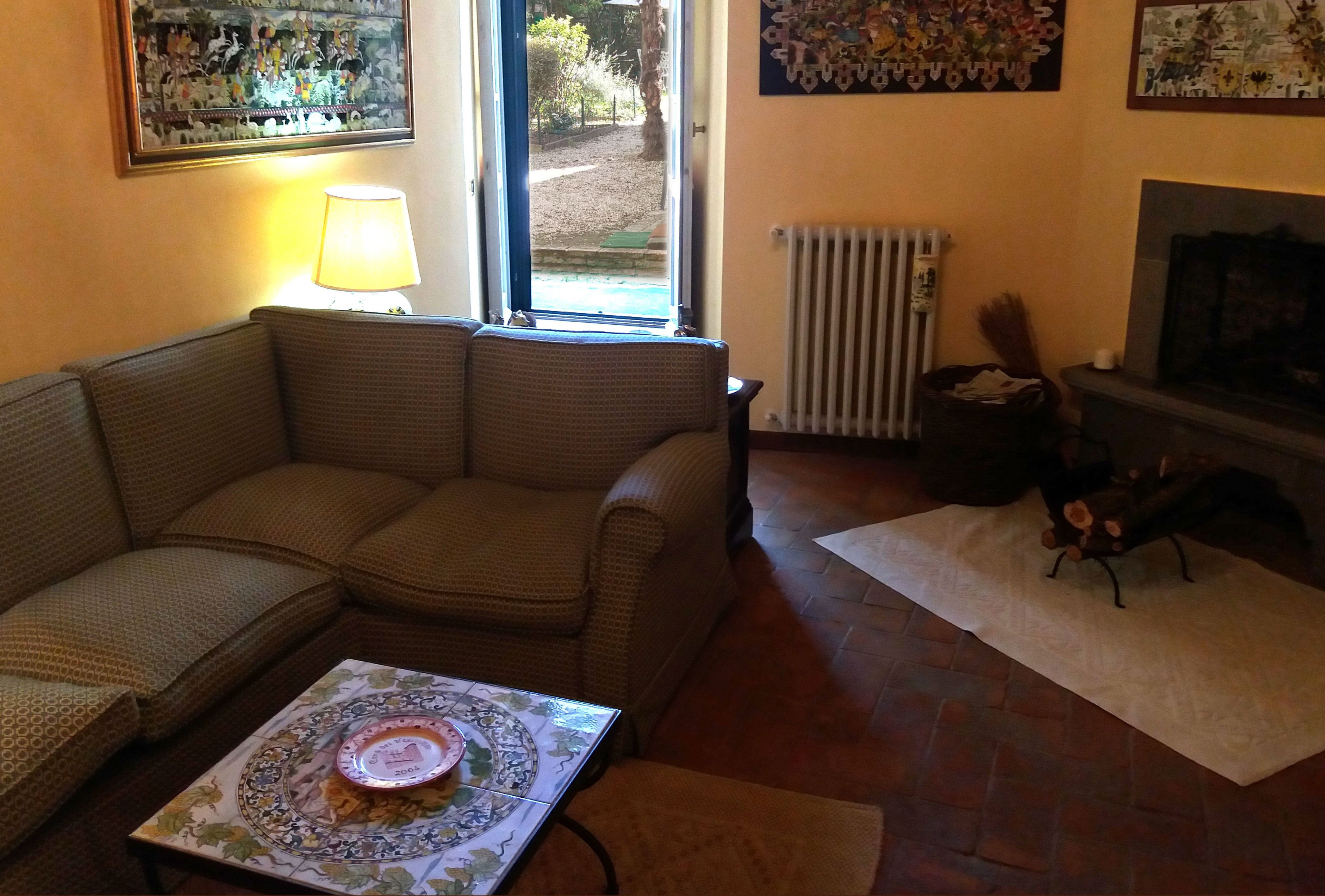 A living room with a sofa, a table with a decorative plate, a fireplace, and a window with a view of the outdoors.
