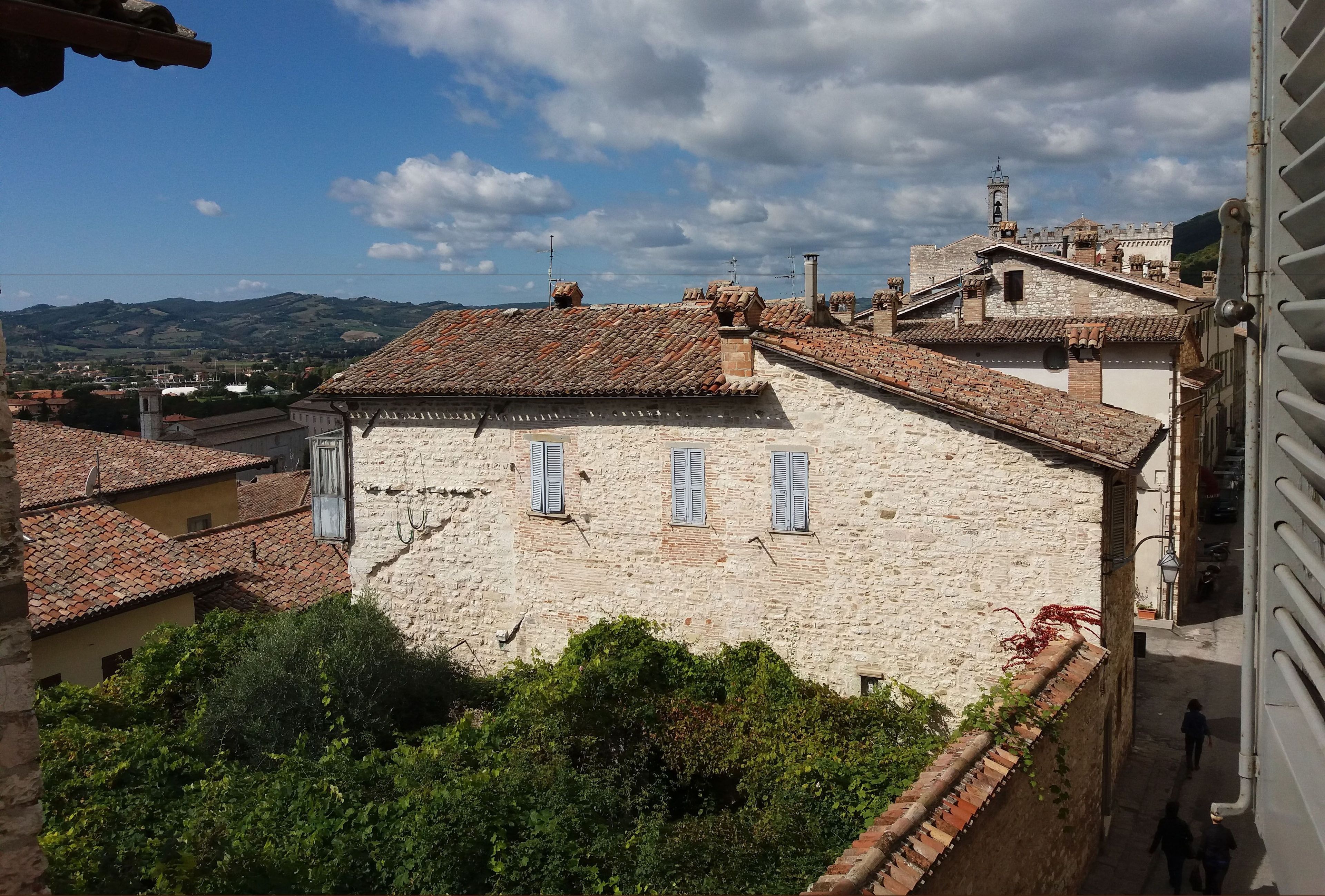 A stone building with a tiled roof, a bell tower, and a view of distant hills.