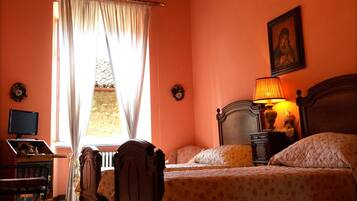 A bedroom with a wooden bed, a nightstand with a lamp, a chair, a desk, and a window with curtains.