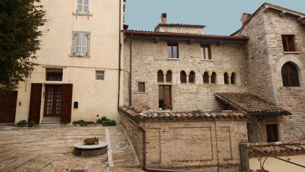 Un patio con edificios de piedra, una puerta de madera y una pequeña mesa circular de piedra con una planta.
