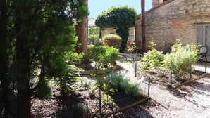 Un jardín con diversas plantas y árboles, un edificio de piedra y una valla de madera.