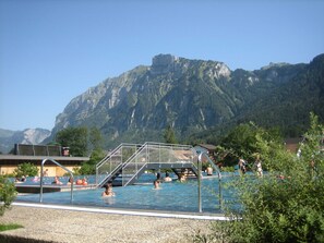 Una piscina con una escalera metálica que da al agua, rodeada de árboles y montañas al fondo.