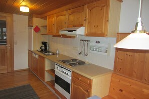 Una cocina con armarios de madera, estufa, cafetera y lámpara colgante.