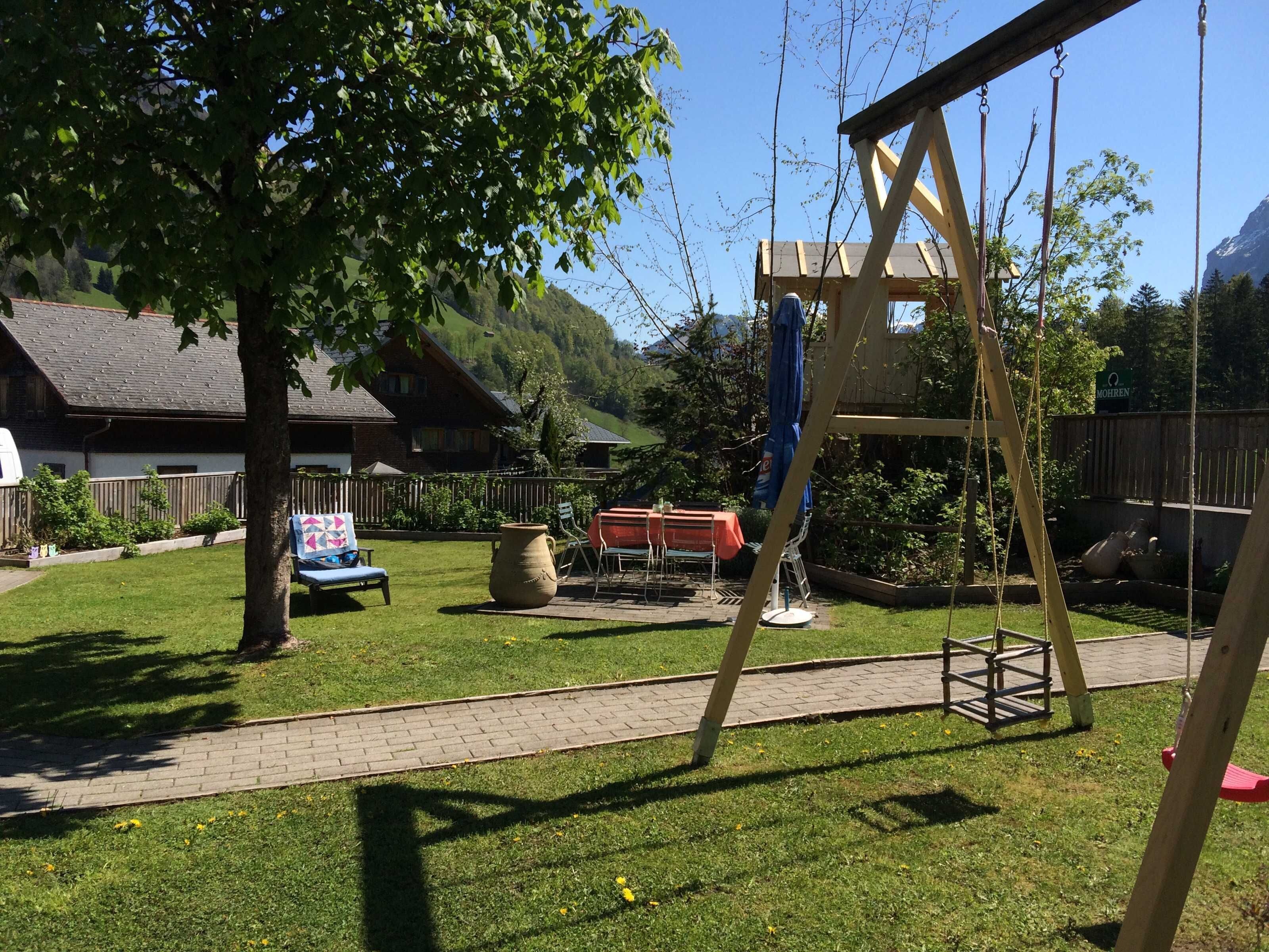 Een achtertuin met een schommel, een tafel met stoelen en een grote pot.