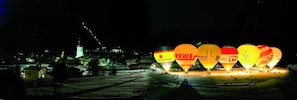 Cena noturna com balões de ar quente iluminados e um edifício iluminado ao fundo.