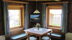 Una habitación con paredes de madera, una mesa con sillas, un televisor y ventanas con cortinas.