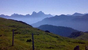 Una colina cubierta de hierba con una valla y montañas a lo lejos.